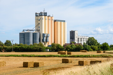 Two grain tower silos in the countryside, a smaller and older gray one next to a more recent and...