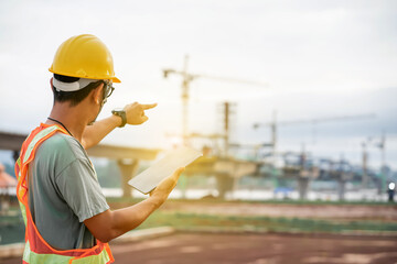 Asian male engineer using laptop and drone to inspect construction at bridge construction site. Construction area of ​​large bridge connecting road across river.