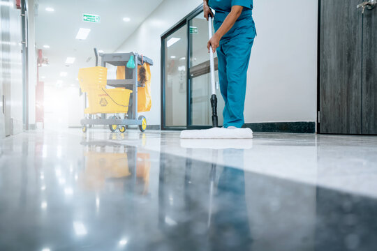 A Safety sign with caution phrase. Happy young housekeeper mopping the floor with a mop and cleaning products to clean dust in a hospital corridor.