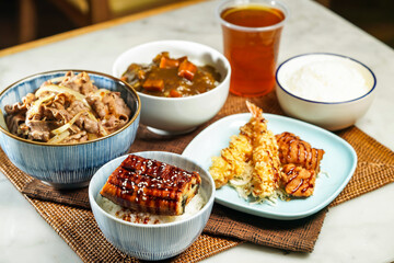 Assorted japanese food verity Teriyaki eel donburi with rice, UMAI Beef Donburi, Deep Fried Chicken and Deep Fried Shrimp Curry rice, and iced tea served on table side view of asian food