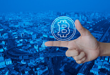 Bitcoin icon on finger over modern city tower, street, expressway, and skyscraper , Internet currency concept