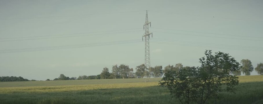 A tall power line tower stands in a field. The sky is overcast and the grass is green