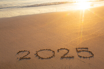 Written text 2025 on the sea beach at sunrise.