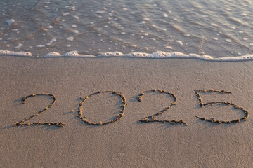 Written text 2025 on the sea beach at sunrise.