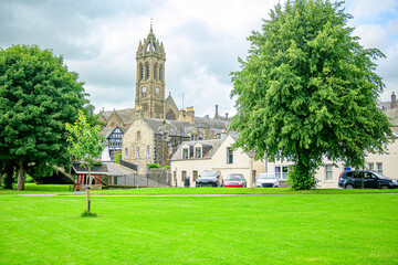 Fototapeta premium Public park along the banks of the river Tweed in Peeples a village in the Borders region of Scotland with parked cars and a stone church spire in the background. 