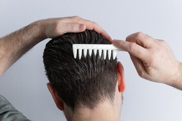 Head shot from behind of a man with gray hair combing his hair with a white comb. Isolated on gray background. Concept of hairstyle and hair care