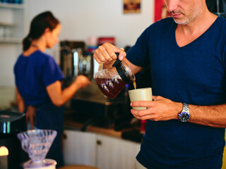 Barista pours freshly brewed coffee into a mug in a café setting, showcasing the process of serving a quality beverage and emphasizing the art and care involved in coffee preparation.