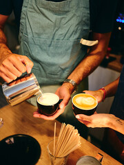 A barista pours milk into a coffee cup as another barista holds a different cup, capturing the collaborative effort and skill in making perfect coffee in a busy cafe environment.