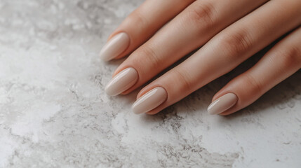 Close-up shot of well-maintained, healthy nails on a hand resting on a light, neutral-colored surface. The nails are clean, smooth, and neatly trimmed, with a natural shine. The skin around 