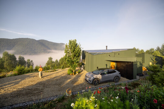 A serene morning scene with mist rolling over the mountains, a modern cabin, and an electric car parked in front, representing sustainable living in harmony with nature