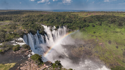Fototapeta premium Kalandula Waterfall cascading beautifully in Angola with a rainbow forming in the mist under a clear blue sky