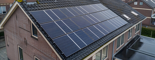 Obraz premium A photovoltaic panel is mounted on the roof of an old house in the Dutch style, which has been covered with black solar panels