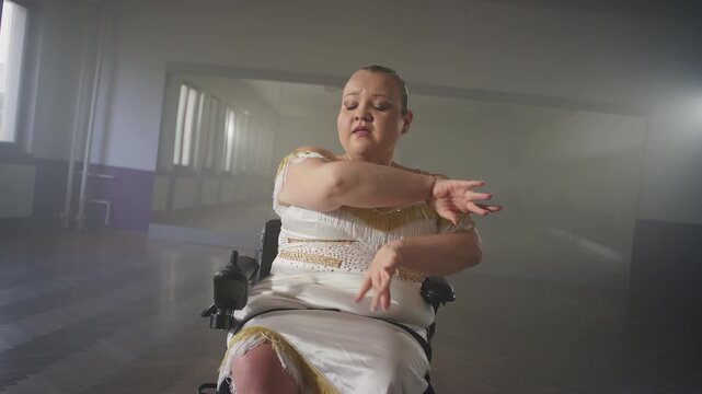 Young smiling woman with a disability enjoying making elegant graceful moves while dancing in a wheelchair, para dance medium close up shot.
