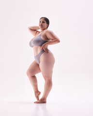 Full-length portrait of overweight woman posing in grey lingerie, shows her confidence against...