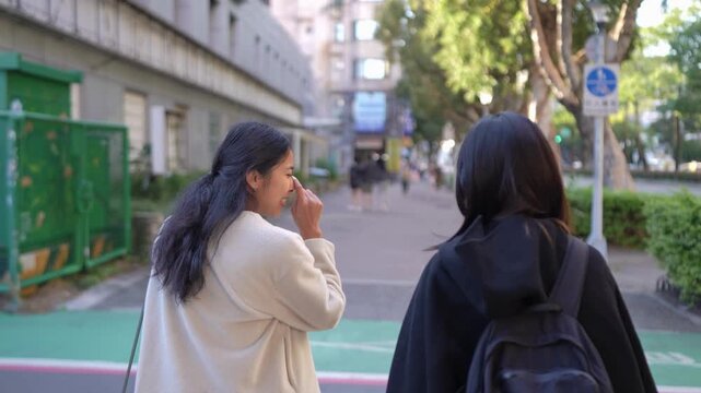 A slow-motion video capturing a young Taiwanese woman and a South Asian woman walking and chatting amiably on a public road near a university in Taipei's Da'an District.