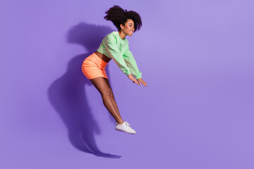 Full body length photo of young funny energetic flying girl with wavy hair in green top and orange mini skirt isolated on violet color background