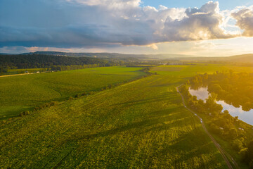 The golden hour sun casts a warm glow over a sprawling landscape with a meandering river, green...