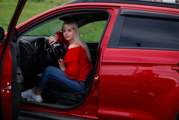 Young, attractive pretty blonde girl in new red car, smiling and looking satisfied with her life