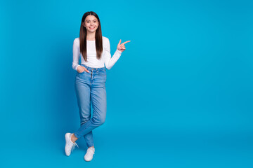 Full length photo of lovely teen lady posing model point empty space dressed stylish white garment isolated on blue color background