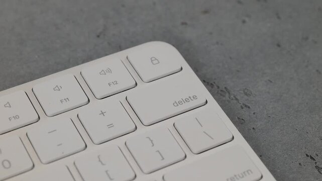 Man pressing delete button on white keyboard on grey background
