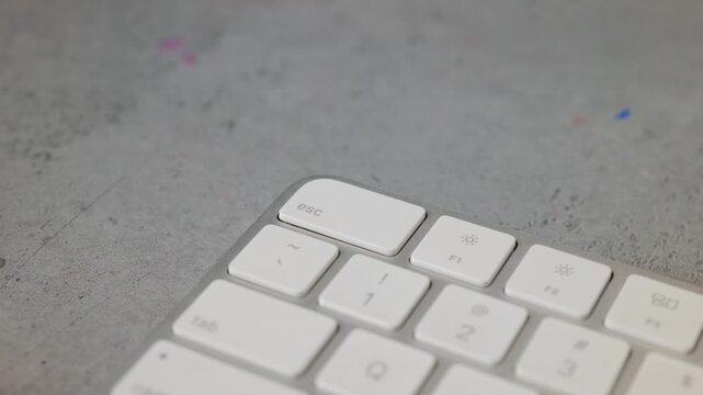 Man pressing esc button on white keyboard on grey background	

