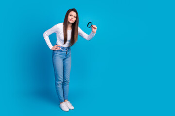 Full body photo of attractive teen woman skeptical look magnifier loupe dressed stylish white clothes isolated on blue color background