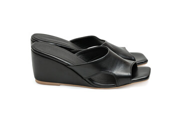 A pair of modern fashionable women's black leather wedge sandals shoe has a low, angled heel and an open-toe design isolated on a white background.