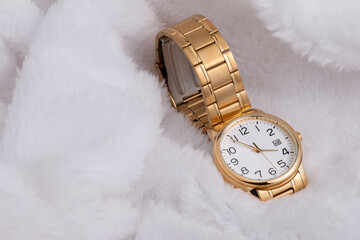 Luxury wristwatch made of a gold-toned metal on a white background, with depth of field. Close-up