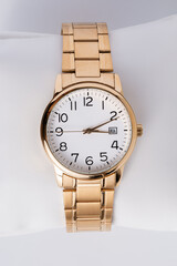 Luxury wristwatch made of a gold-toned metal on a white background, with depth of field. Close-up