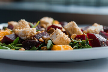 Vegetable salad with arugula, cheese, orange and beets on a white plate