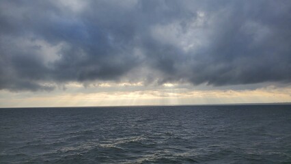 A serene seascape under a brooding sky, where rays of light pierce through clouds to touch the ocean, creating a tranquil and mesmerizing scene.