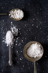 Top view of a spoons with coarse grained sea salt on black background. Flat lay. Top view. Food concept.