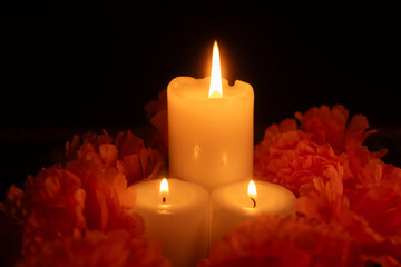 A striking arrangement of three candles surrounded by marigolds, with a black background and Day of the Dead cloth