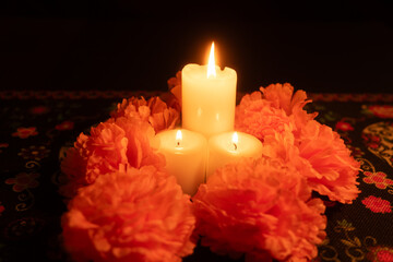 Three glowing candles surrounded by bright orange marigolds on a black background