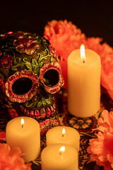 Vertical image featuring a skull decked with metallic flowers and surrounded by bright orange marigolds and candles