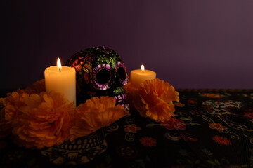 A skull embellished with metallic flowers, with two candles burning on each side. Orange flowers and additional lit candles are placed around