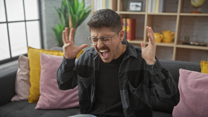 A young hispanic man shouts in excitement indoors, showcasing a homely, comfortable living room...