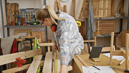 A focused blonde woman measures wood in a well-equipped carpentry workshop, embodying diy and craftsmanship.