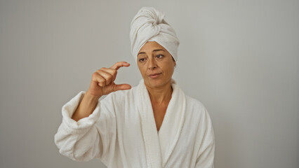 Mature hispanic woman in a bathrobe with a towel on her head making a small size gesture isolated on a white background