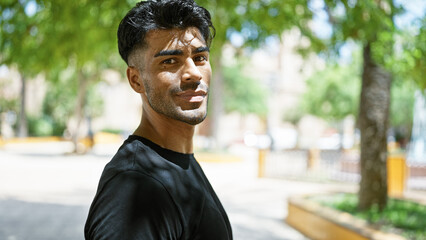 Handsome hispanic man with beard smiling outdoors in a sunny green park