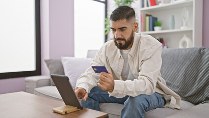 A bearded man shops online with a credit card in a cozy living room setting.