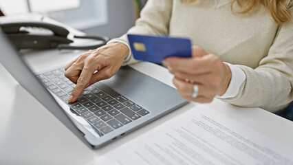 Professional woman typing on laptop and holding credit card in a modern office setting