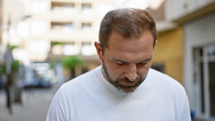 Obraz premium Mature hispanic man with grey hair in an urban setting looking thoughtfully downward.