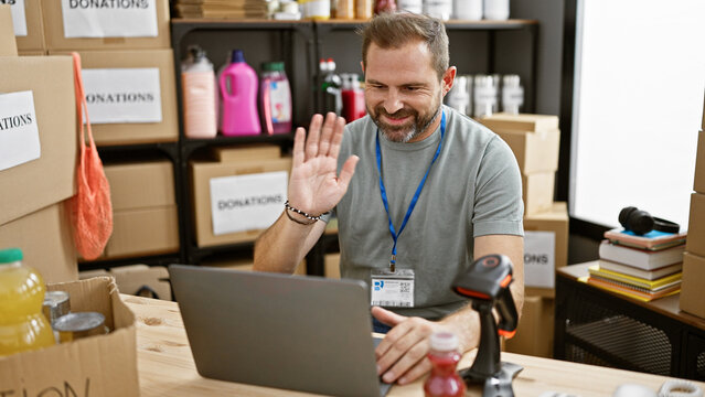 Handsome hispanic man in a warehouse with donations gestures at a laptop during a video call.
