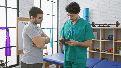 Obraz premium Physiotherapist in scrubs using tablet with male patient in a modern rehab clinic room