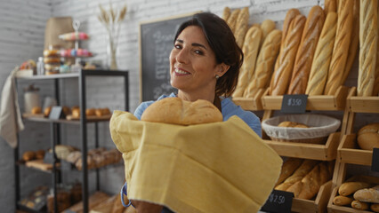 Woman smiling holding fresh bread in a bakery filled with various baked goods and baguettes displayed on shelves in the background