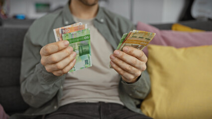 A young hispanic man holds norwegian currency kroner in his home, conveying a sense of personal finance or travel preparation.