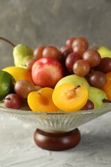 Glass vase with different fresh fruits on gray textured table, closeup