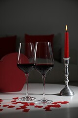 Burning candle, wine in glasses and paper hearts on table indoors