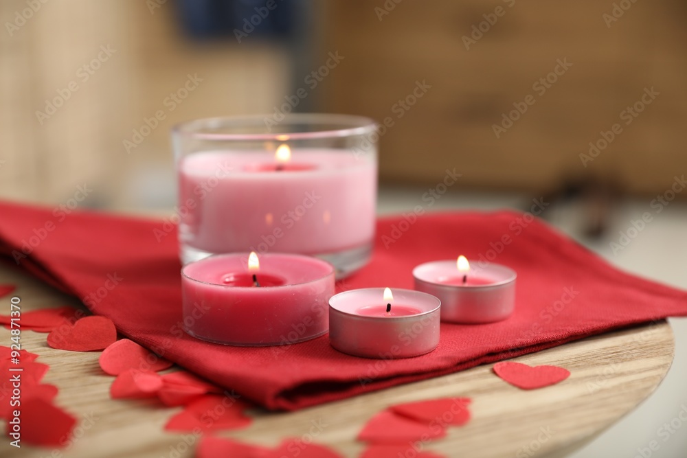 Poster Burning candles, napkin and red paper hearts on wooden table indoors, closeup